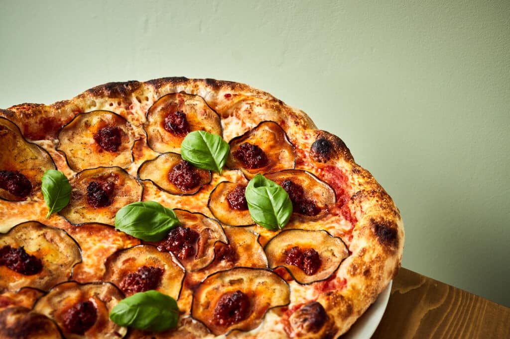 Czy kuchnia włoska jest zdrowa? Sekret tkwi w prostocie. Na zdjęciu pizza z bakłażanem i bazylią na oliwkowym tle.