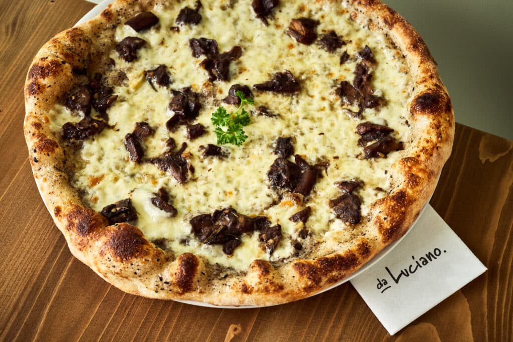 Pizza bianca z mozzarellą na drewnianym stole. Obok serwetka z napisem restauracja da Luciano.