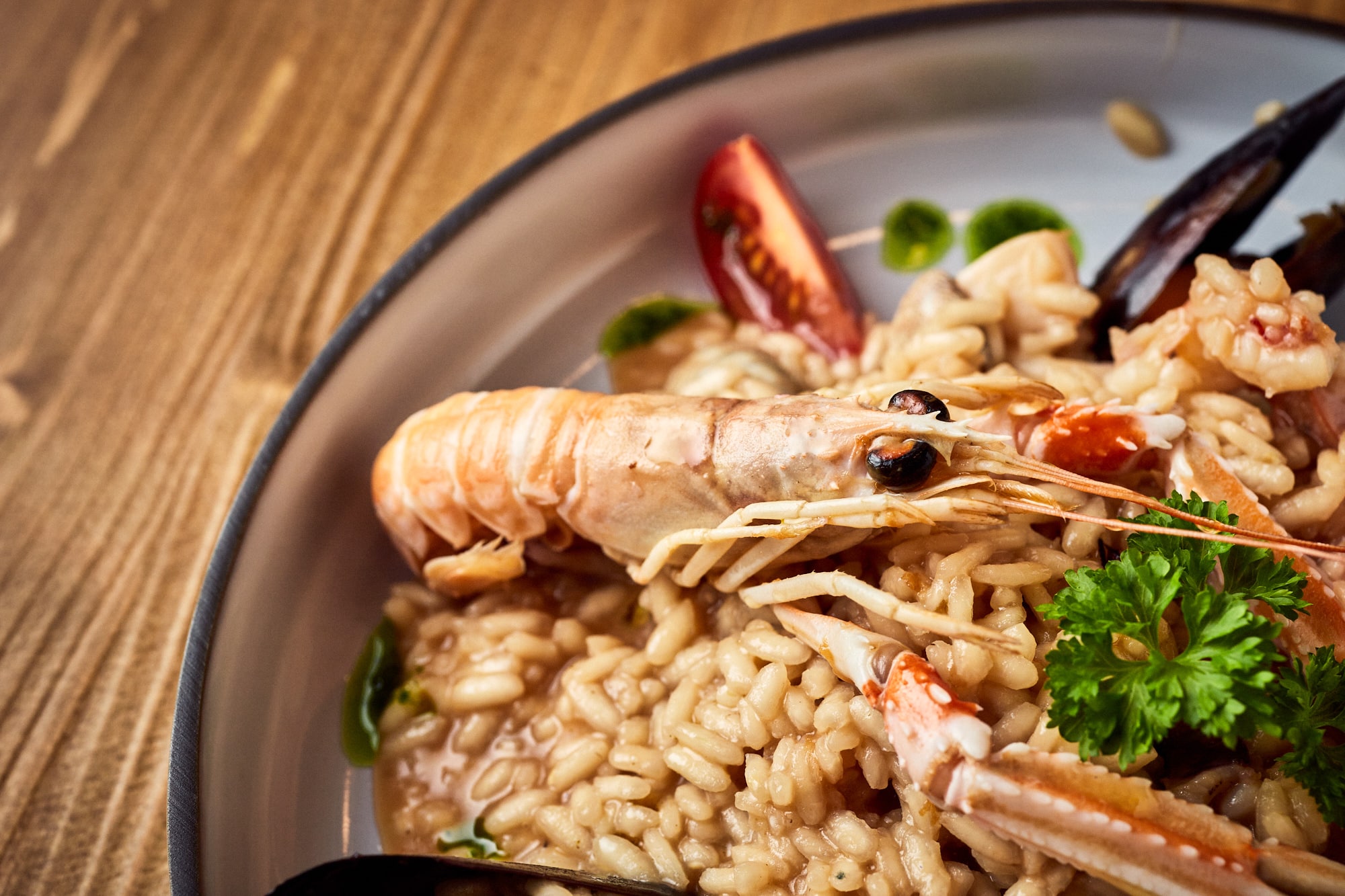 Aromatyczne risotto z owocami morza, w tym duże krewetki argentyńskie, podane w półgłębokim talerzu.