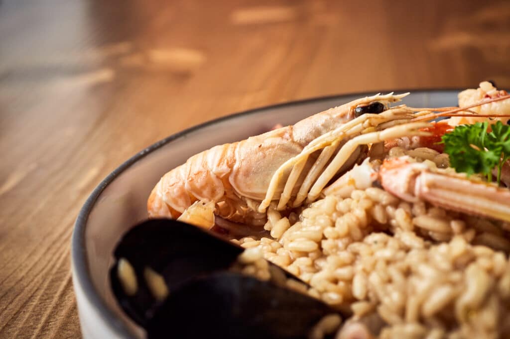 Włoskie risotto z owocami morza podane w talerzu z ciemną obwódką na drewnianym stole.